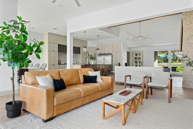 living room featuring ceiling fan with notable chandelier, light wood finished floors, and a high ceiling