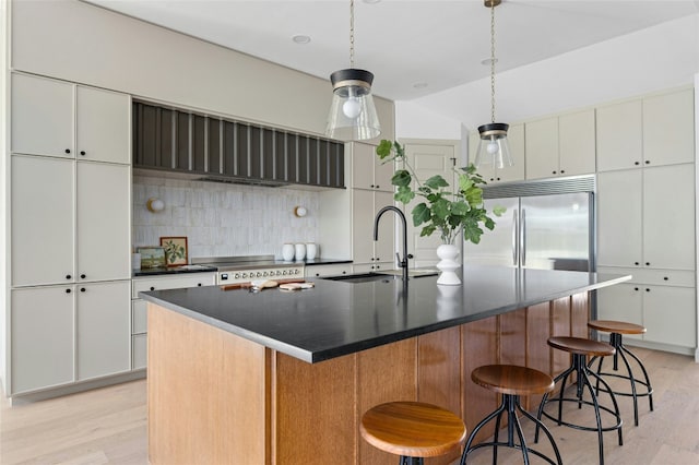 kitchen featuring built in refrigerator, dark countertops, light wood-style flooring, and a sink