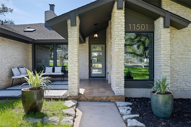 entrance to property with a chimney, a porch, and roof with shingles