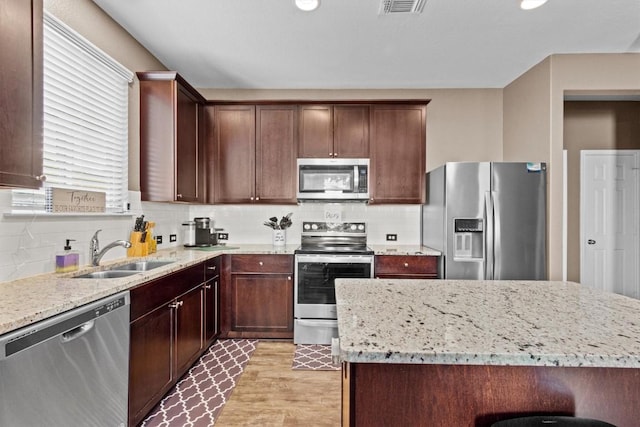 kitchen featuring decorative backsplash, appliances with stainless steel finishes, light stone counters, light wood-style floors, and a sink