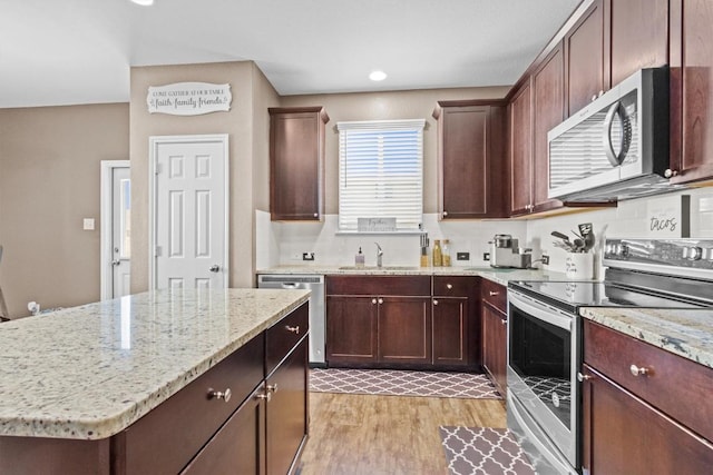 kitchen with light wood finished floors, appliances with stainless steel finishes, a sink, a kitchen island, and light stone countertops