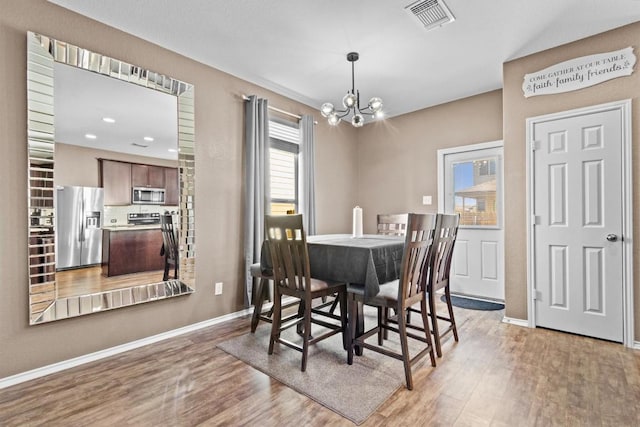 dining space with light wood finished floors, baseboards, visible vents, and a notable chandelier