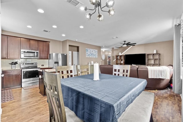 dining area with light wood-style flooring, visible vents, and ceiling fan with notable chandelier