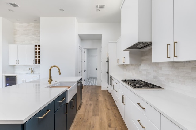 kitchen with stainless steel appliances, white cabinets, custom range hood, and visible vents