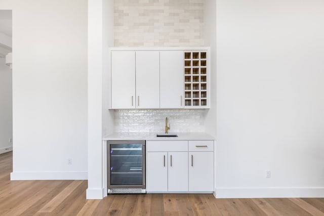 bar featuring wine cooler, indoor wet bar, tasteful backsplash, a sink, and baseboards