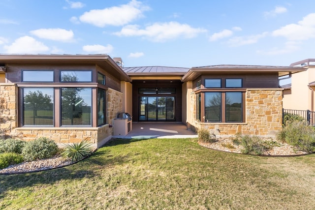 rear view of house with a patio, a lawn, a standing seam roof, metal roof, and stone siding