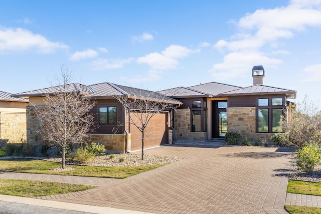 prairie-style house featuring metal roof, stone siding, a standing seam roof, and an attached garage