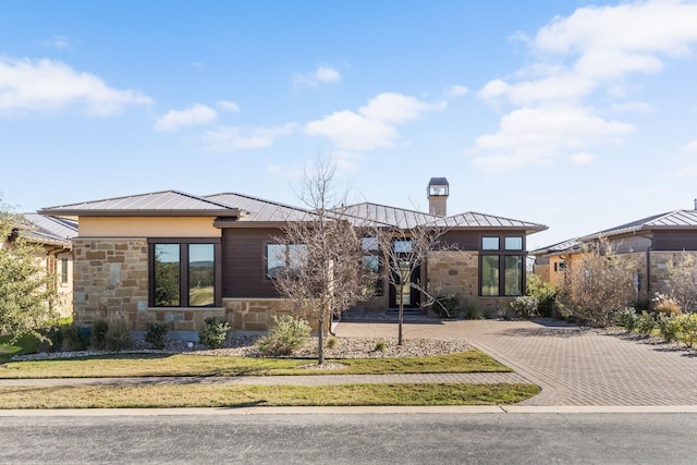 prairie-style house featuring stone siding, a chimney, metal roof, and a standing seam roof