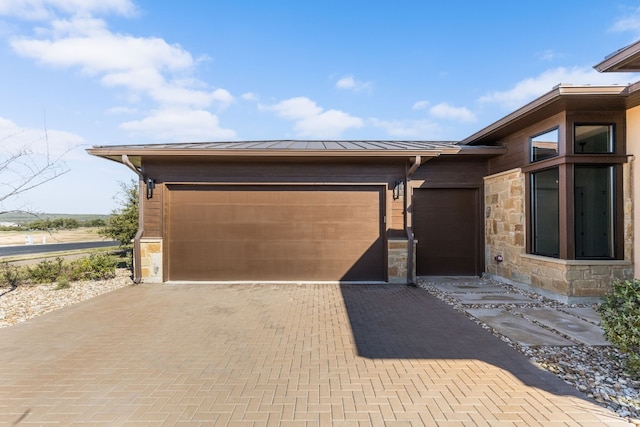 view of home's exterior featuring decorative driveway, a standing seam roof, metal roof, a garage, and stone siding