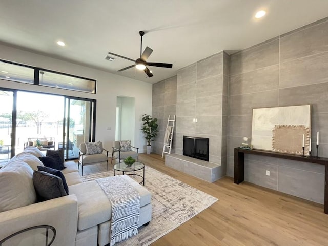 living room with a ceiling fan, a tile fireplace, light wood-type flooring, tile walls, and recessed lighting