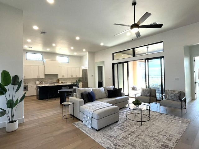 living area featuring light wood finished floors, baseboards, visible vents, a high ceiling, and recessed lighting