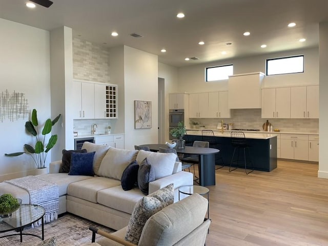 living area with light wood-style floors, a high ceiling, visible vents, and recessed lighting