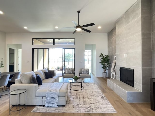 living room featuring a ceiling fan, a tiled fireplace, light wood-style flooring, and recessed lighting