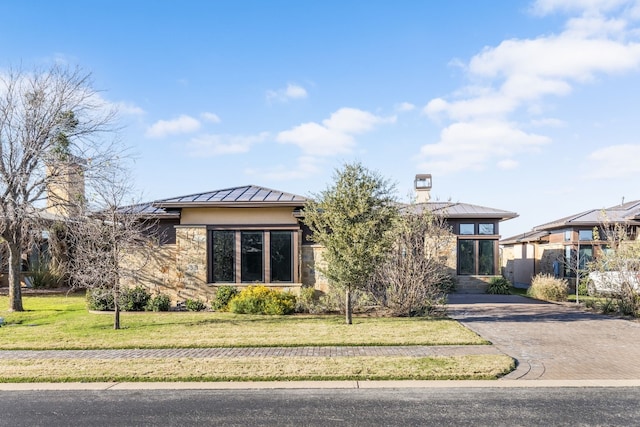 prairie-style home with decorative driveway, stucco siding, a standing seam roof, metal roof, and a front lawn