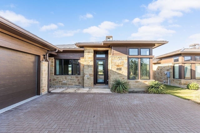 view of front facade with decorative driveway, a standing seam roof, metal roof, a garage, and stone siding