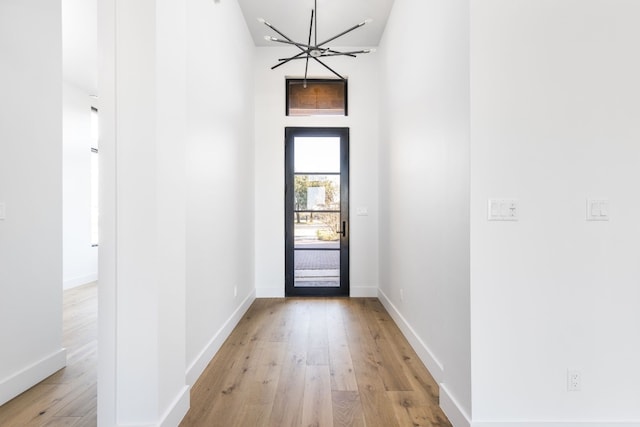 doorway to outside featuring a towering ceiling, light wood-style flooring, a chandelier, and baseboards