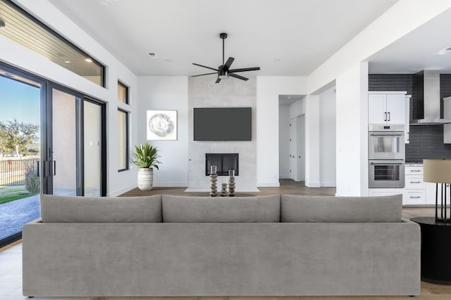 living area featuring light wood-type flooring, a tile fireplace, a ceiling fan, and baseboards