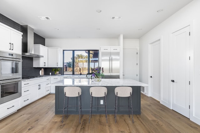 kitchen featuring stainless steel appliances, visible vents, a kitchen island, wall chimney range hood, and wood finished floors