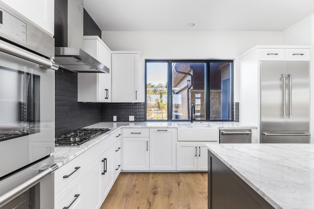 kitchen featuring wall chimney exhaust hood, appliances with stainless steel finishes, white cabinetry, and decorative backsplash