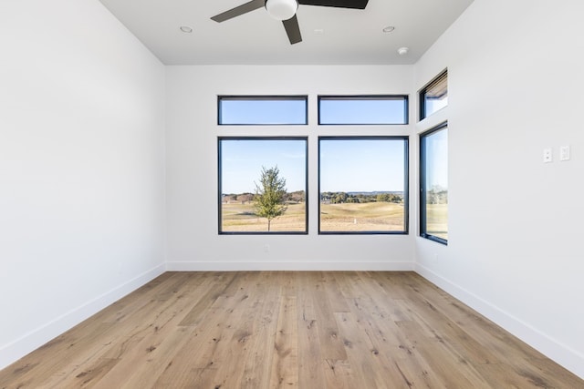 empty room featuring light wood-style floors, a ceiling fan, a wealth of natural light, and baseboards