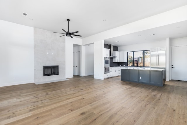 unfurnished living room with baseboards, visible vents, ceiling fan, light wood-type flooring, and a fireplace