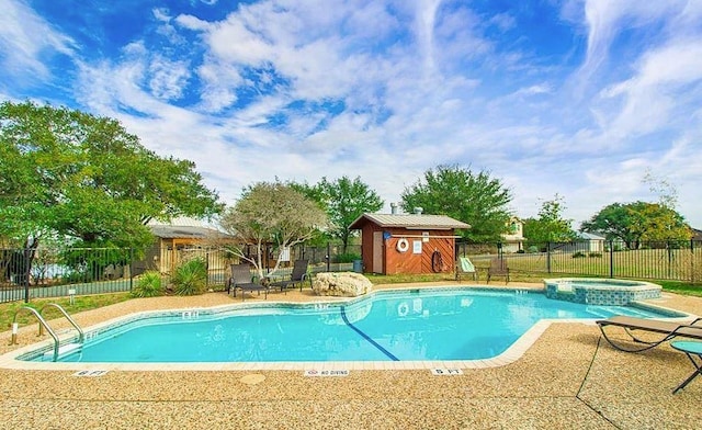 view of swimming pool with an outbuilding, a pool with connected hot tub, a patio area, fence, and a shed