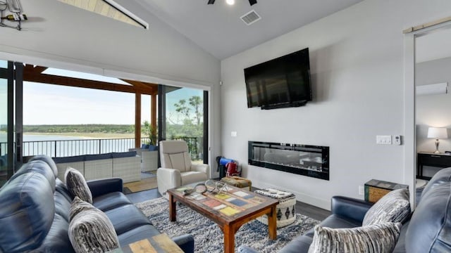 living room with wood finished floors, visible vents, a ceiling fan, vaulted ceiling, and a glass covered fireplace