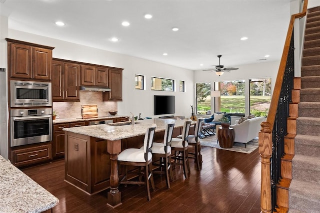 kitchen featuring decorative backsplash, appliances with stainless steel finishes, open floor plan, a sink, and under cabinet range hood