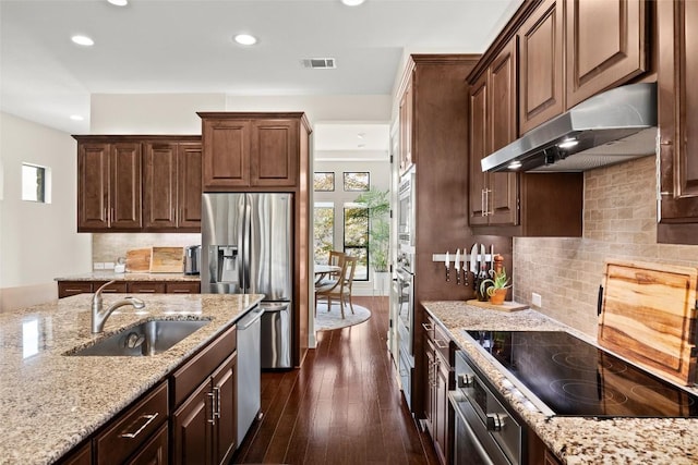 kitchen featuring stainless steel appliances, visible vents, a sink, light stone countertops, and under cabinet range hood