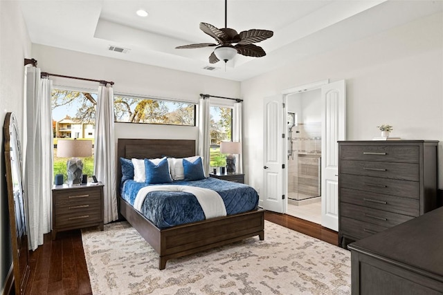 bedroom featuring connected bathroom, visible vents, a tray ceiling, and wood finished floors