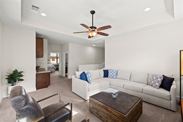 living area with a tray ceiling, visible vents, light carpet, and ceiling fan