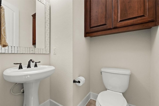 half bath with toilet, baseboards, and a sink