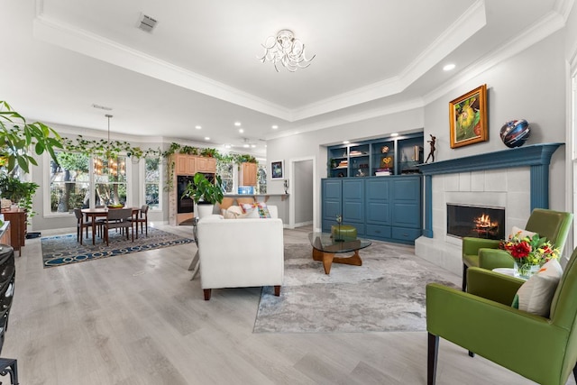 living area featuring a notable chandelier, a raised ceiling, visible vents, light wood-type flooring, and a tile fireplace