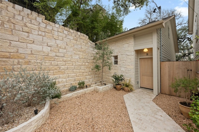 view of exterior entry featuring stone siding and fence