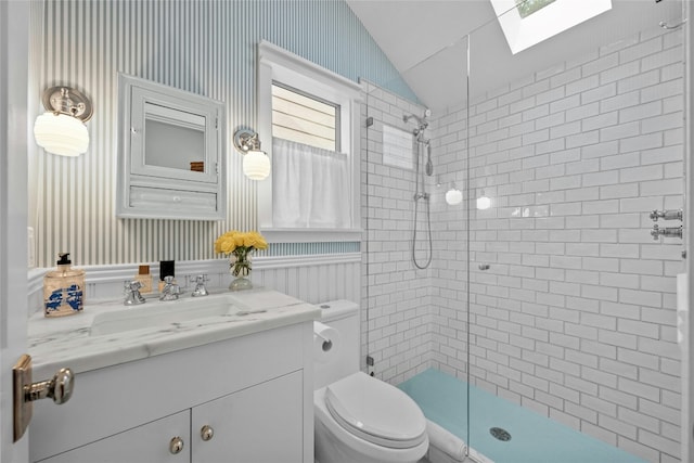 bathroom with vaulted ceiling with skylight, toilet, a wainscoted wall, a tile shower, and vanity