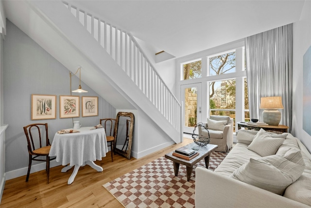 living room with light wood-type flooring, a high ceiling, baseboards, and stairs