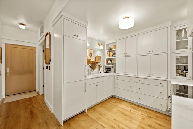 kitchen with white cabinets, glass insert cabinets, and light wood-type flooring