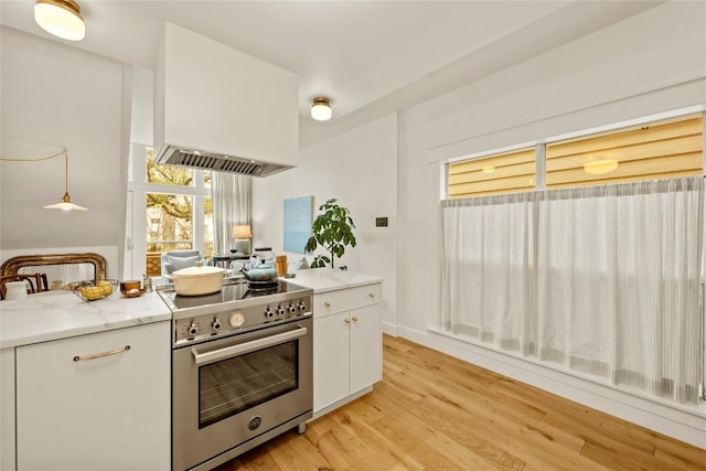 kitchen with light wood-style floors, white cabinets, light stone counters, and high end stainless steel range