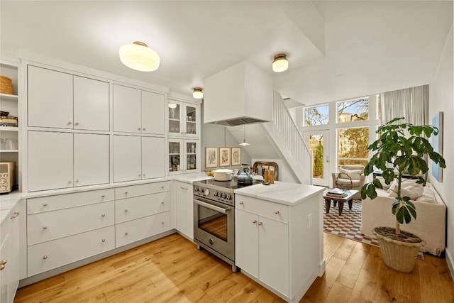 kitchen with premium range hood, light wood-type flooring, a peninsula, high end stainless steel range oven, and white cabinetry