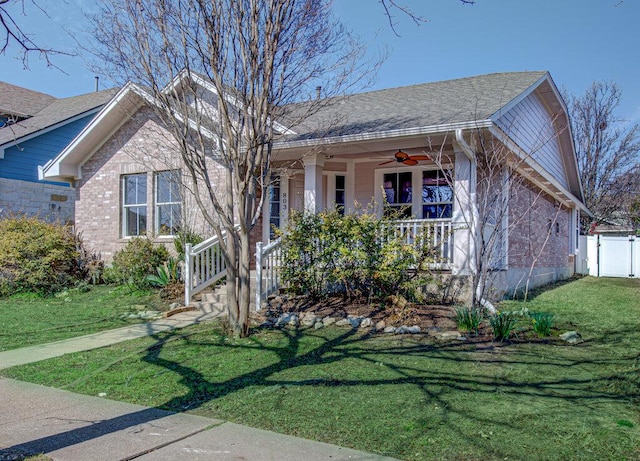 view of front of home with brick siding, a porch, ceiling fan, fence, and a front lawn