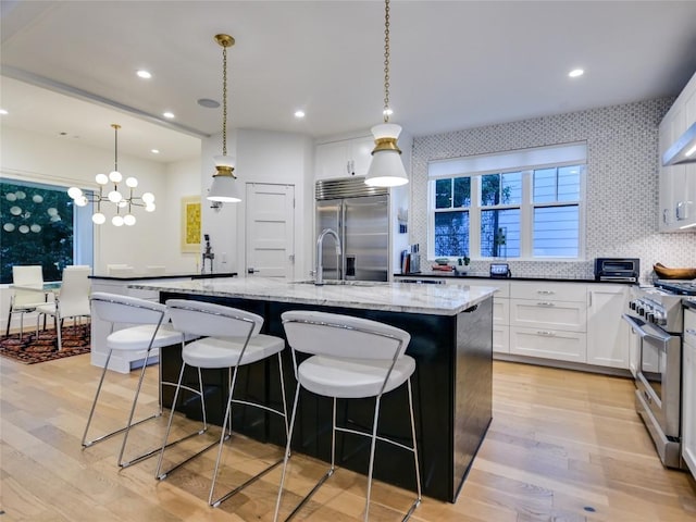 kitchen featuring light wood-style flooring, a kitchen island with sink, light stone counters, and high end appliances