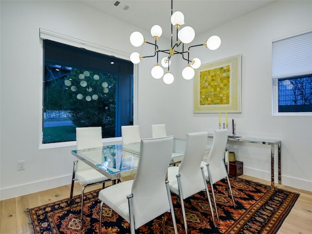 dining area featuring a chandelier, visible vents, baseboards, and wood finished floors