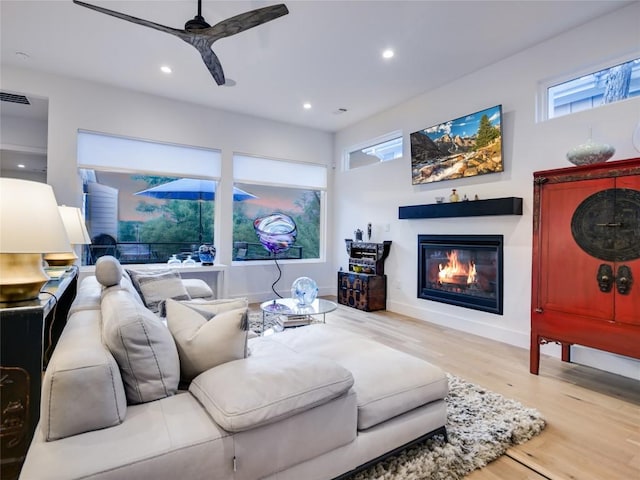 living area with a glass covered fireplace, a healthy amount of sunlight, recessed lighting, and wood finished floors