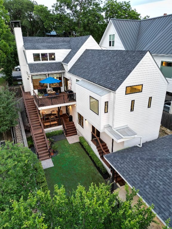 rear view of house featuring a shingled roof, a yard, a chimney, and stairs