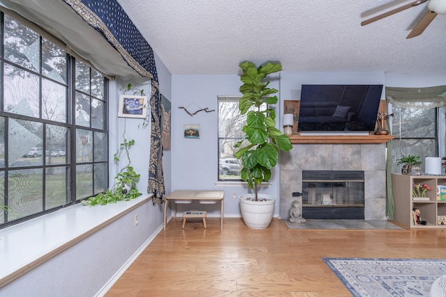 unfurnished living room with a textured ceiling, ceiling fan, wood finished floors, baseboards, and a tiled fireplace