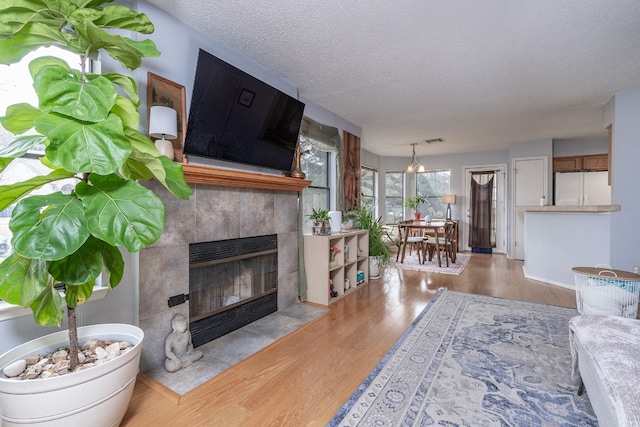 living room featuring visible vents, a tile fireplace, wood finished floors, a textured ceiling, and a chandelier