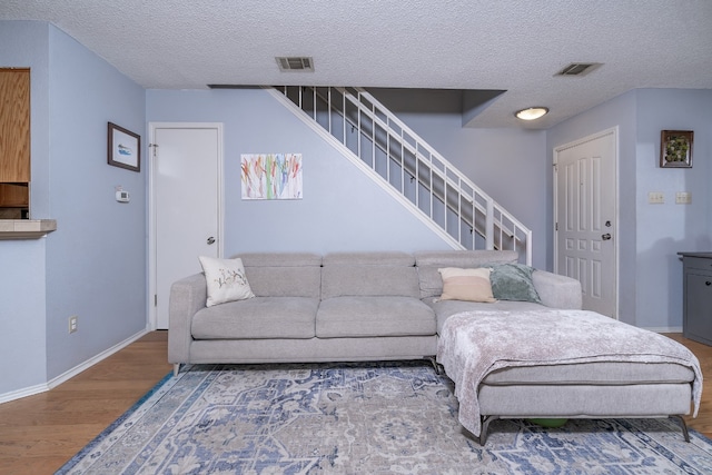 living area featuring visible vents, stairway, a textured ceiling, wood finished floors, and baseboards