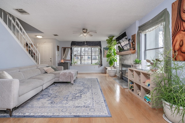 living area featuring visible vents, a glass covered fireplace, ceiling fan, stairway, and wood finished floors