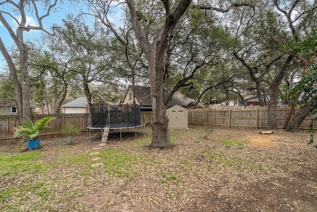 view of yard with a trampoline, an outbuilding, a fenced backyard, and a storage unit