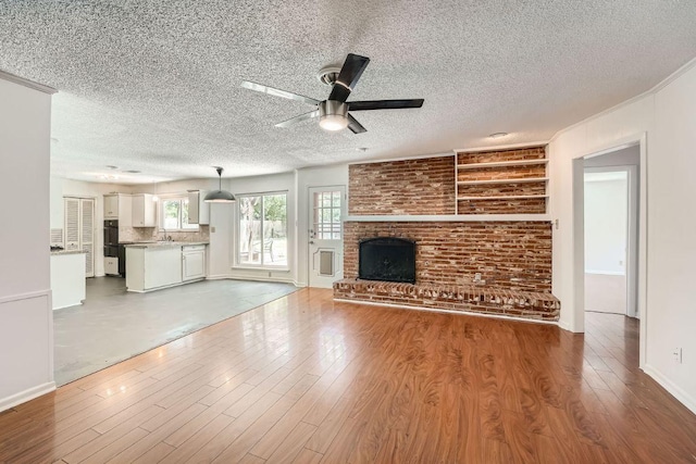 unfurnished living room featuring ceiling fan, a textured ceiling, a brick fireplace, and wood finished floors